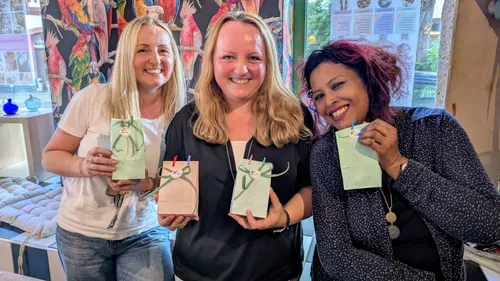 Three women smiling, holding gift bags indoors.