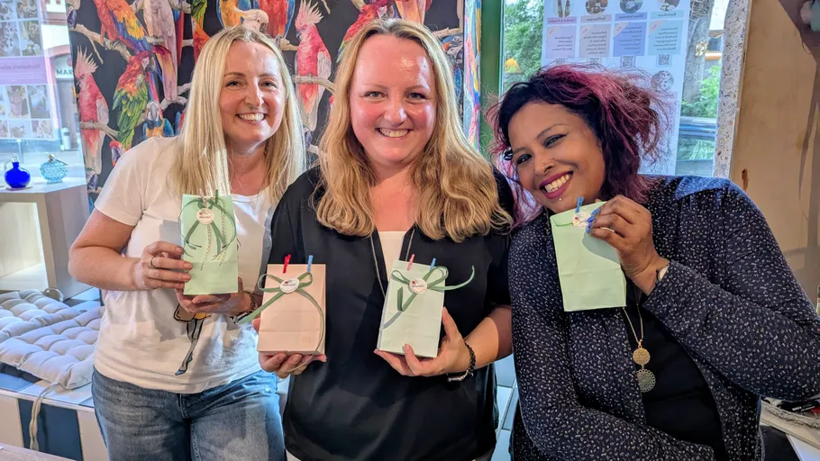 Drei Frauen lächeln, halten Geschenktüten drinnen.