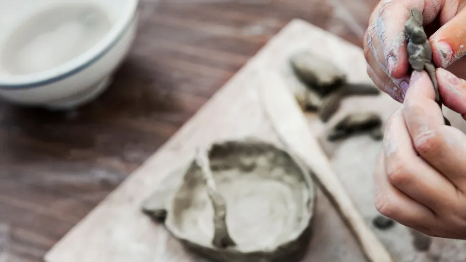 Hands sculpting clay on wooden table.