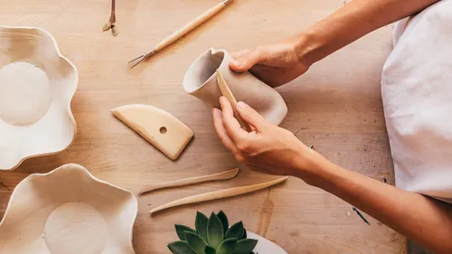 Hands shaping clay with tools on table.