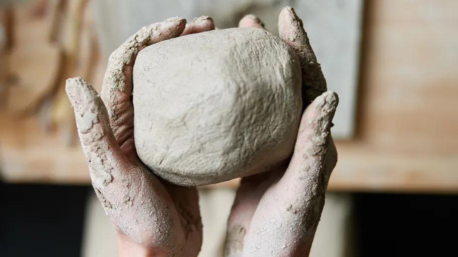 Hands holding a lump of clay indoors.