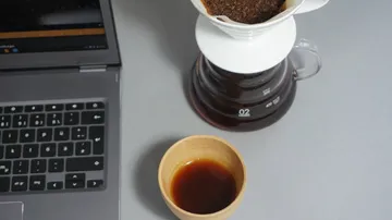 Laptop, coffee cup, and coffee maker on table.