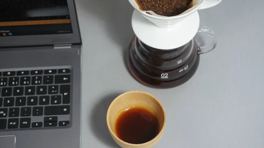 Laptop, Kaffeetasse und Kaffeebereiter auf Tisch.