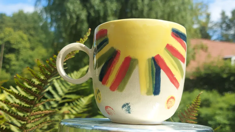 Bunte Tasse auf Tisch im Grünen.