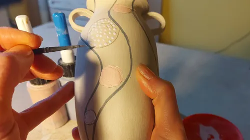 Person malt Designs auf eine Vase.