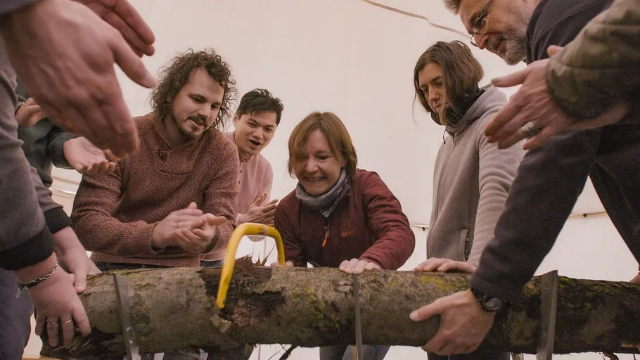 Group using saw to cut log indoors.