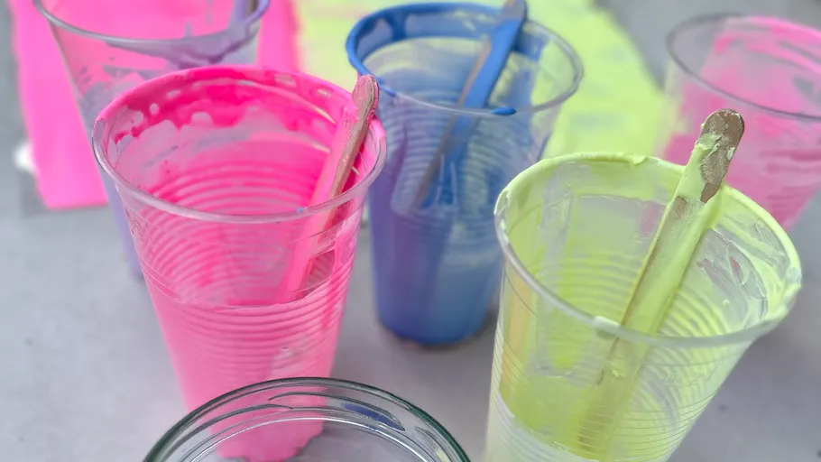 Bunte Farbe in Plastikbechern mit Stäbchen.