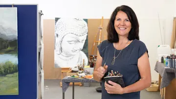 Frau lächelt im Atelier mit Pinseln.