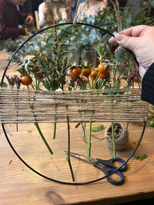 Hand holding floral wreath on wooden table.