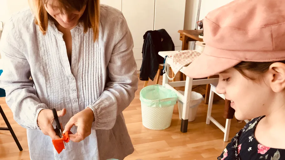 Frau schneidet Stoff, Mädchen schaut zu, im Raum.