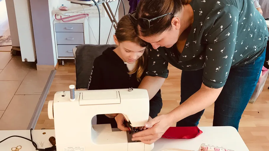 Frau lehrt Mädchen, mit Nähmaschine zu nähen.
