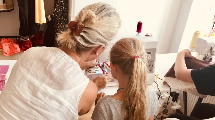 Woman teaching child sewing on machine.
