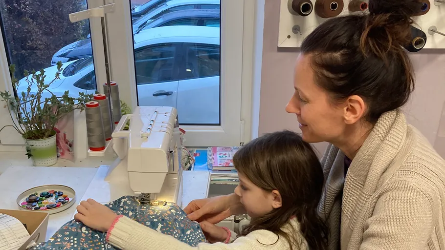Frau und Kind nähen zusammen am Fenster.