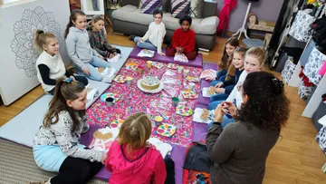 Children seated around colorful picnic indoors.