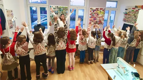 Children with raised hands in sewing classroom.