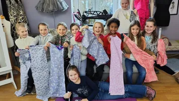Kinder zeigen genähte Kleidung in einem Nähraum.
