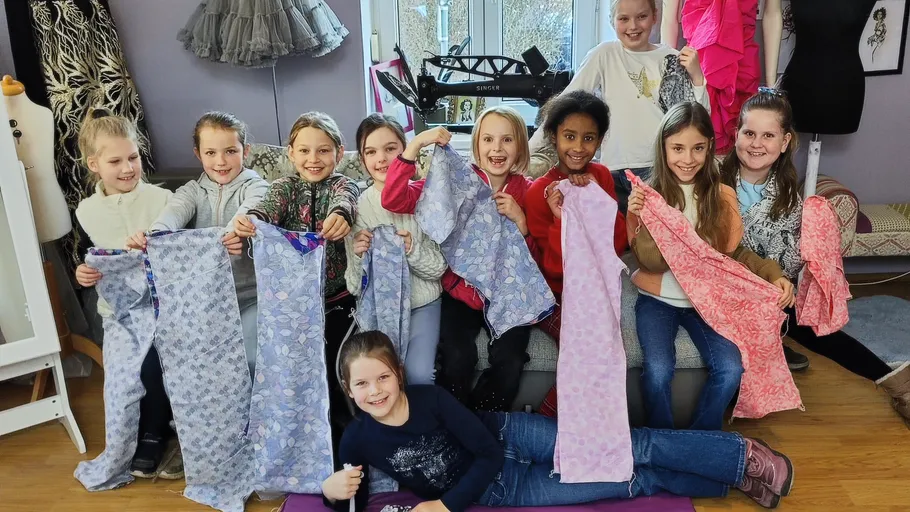 Children displaying sewn garments in a sewing room.