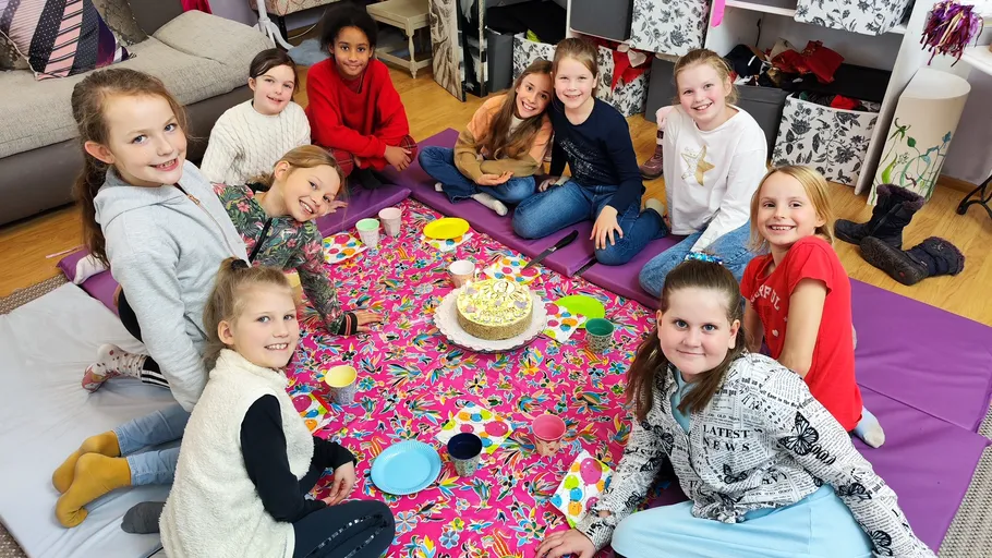 Kinder sitzen um einem dekorierten Kuchen drinnen.