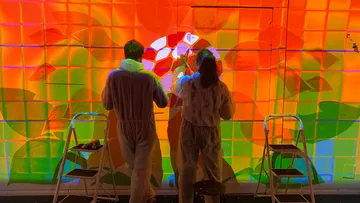 Two people painting colorful wall mural.