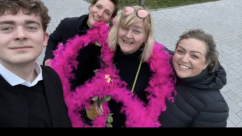 Gruppe von Menschen lächelt draußen mit rosa Boa.
