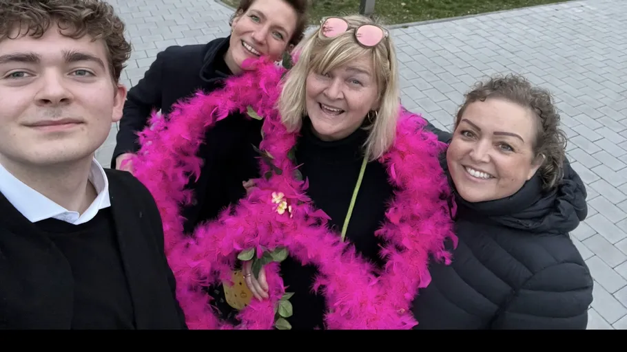 Gruppe von Menschen lächelt draußen mit rosa Boa.