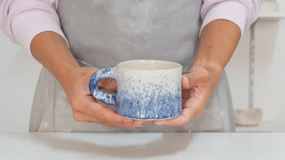 Person hält handgemachte blau-weiße Tasse.