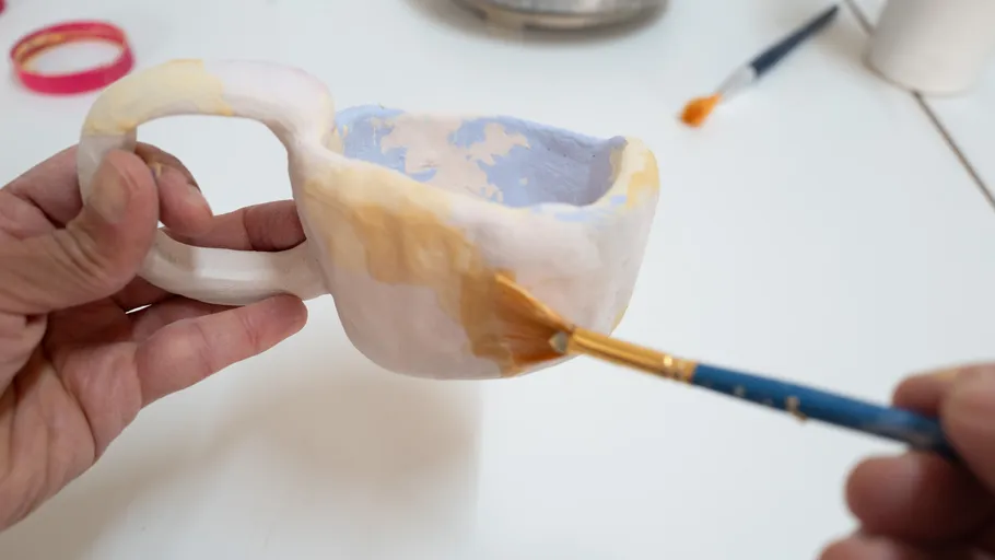 Person painting a handmade mug on table.