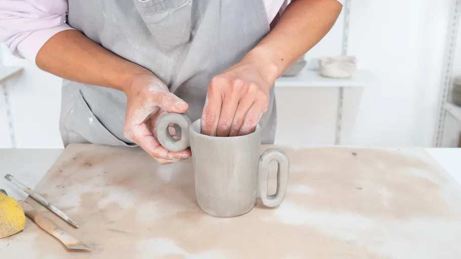 Person shaping clay mug on workshop table.