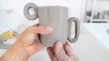 Person hält handgefertigte Tontasse drinnen.