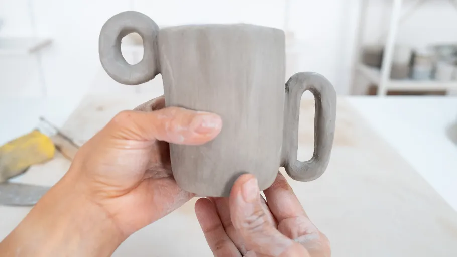 Person holding handcrafted clay mug indoors.