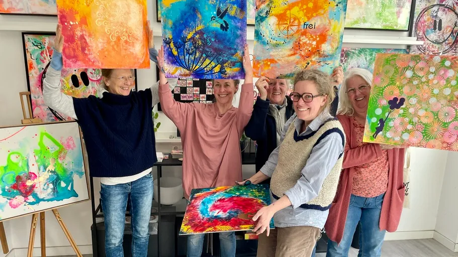 Group holding colorful paintings in an art studio.