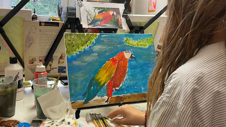 Person painting parrot on canvas indoors.