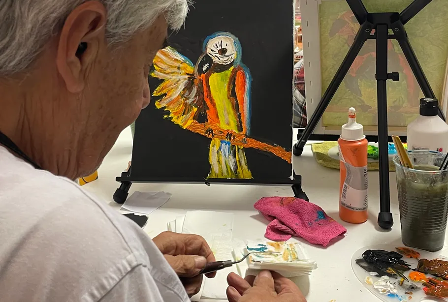 Person painting parrot on canvas, indoor setting.