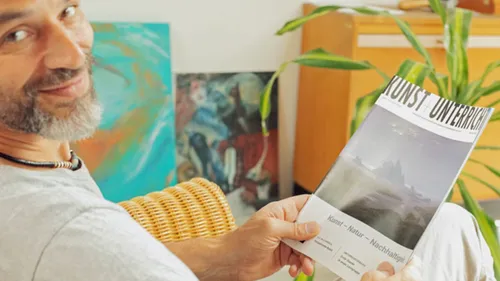 Mann lächelt, hält Kunstzeitschrift drinnen.