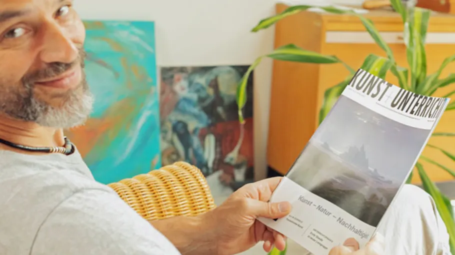 Mann lächelt, hält Kunstzeitschrift drinnen.