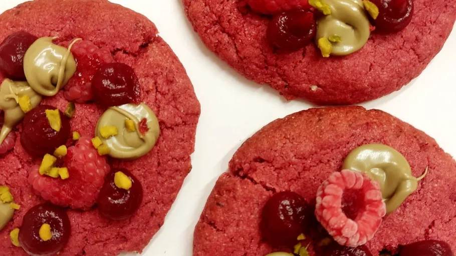 Rote Kekse mit Beeren und Creme belegt.