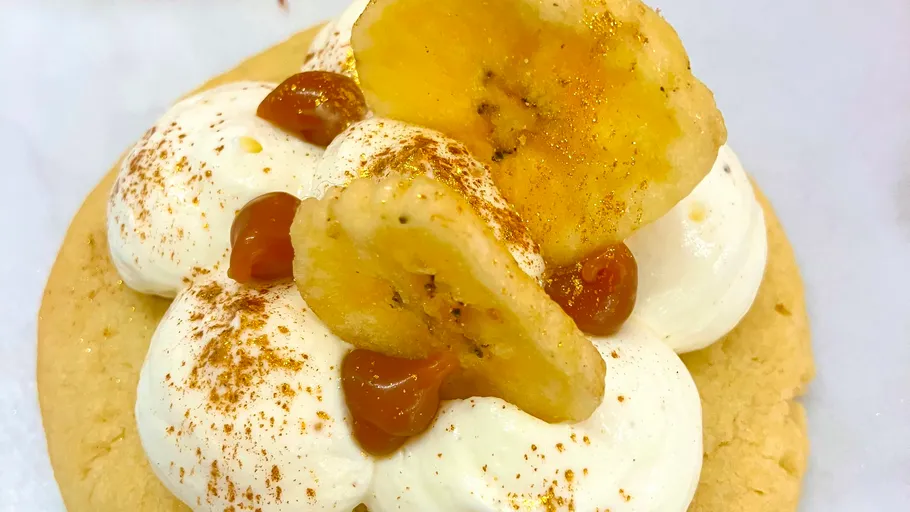 Cookie with cream and banana topping, white plate.