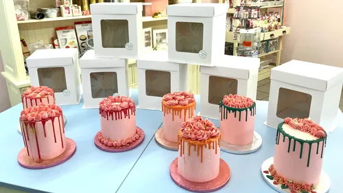 Decorated cakes with icing drips on display table.