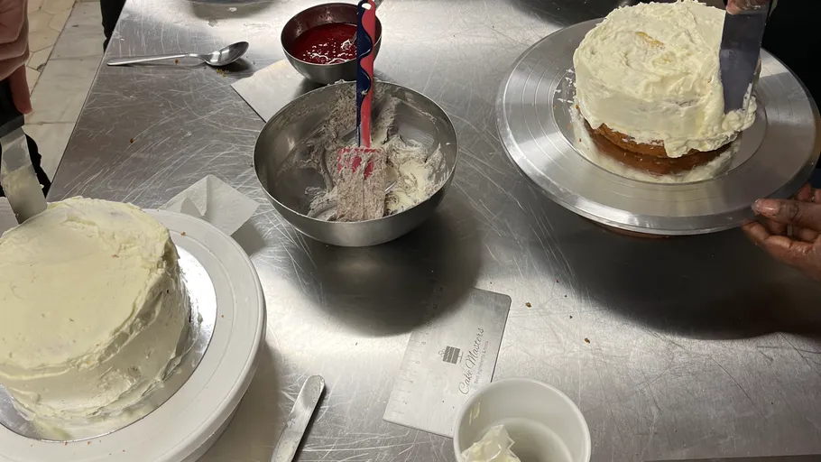 Cakes being frosted on metal counter.