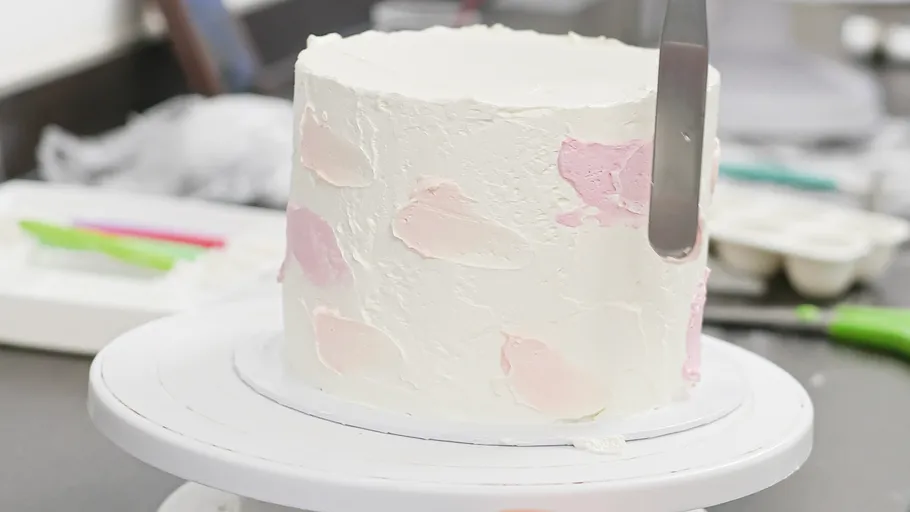 Cake being frosted with pink and white cream.
