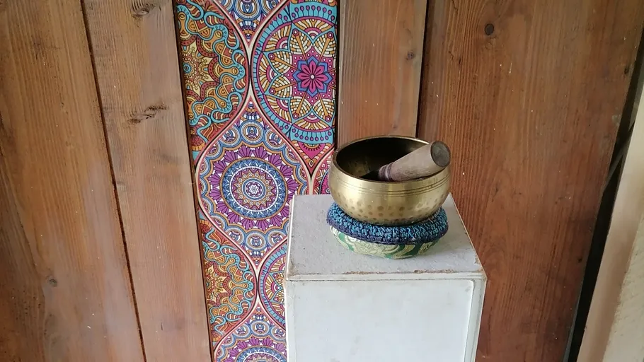 Klangschale auf Sockel, bunter Mandalahintergrund.