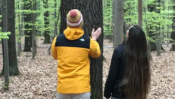 Zwei Personen stehen bei einem Baum im Wald.