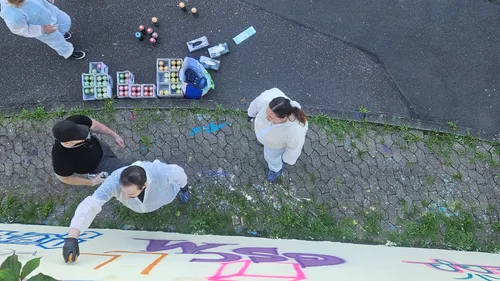 Menschen malen Graffiti an einer Wand draußen.
