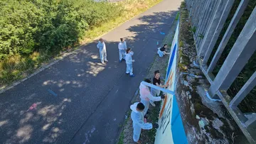 People painting mural on roadside wall.