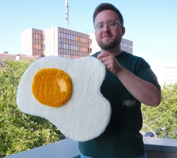 Person hält eiförmigen Teppich auf Balkon.
