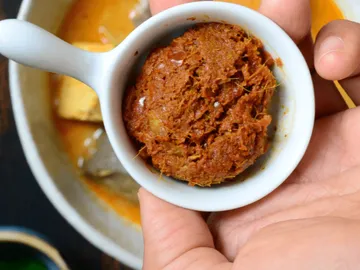 Kleine Schüssel mit einer dicken, würzigen Paste in Hand.