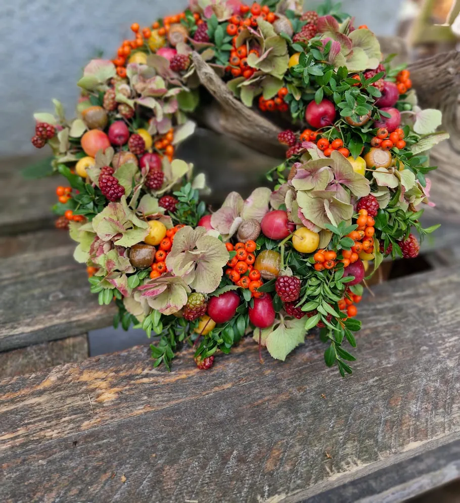 Blumenkranz mit Beeren auf Holzboden.