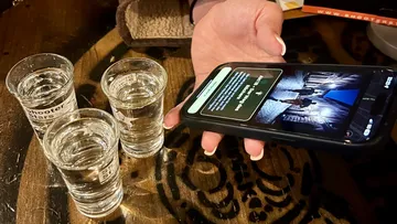 Hand holding phone near three shot glasses.