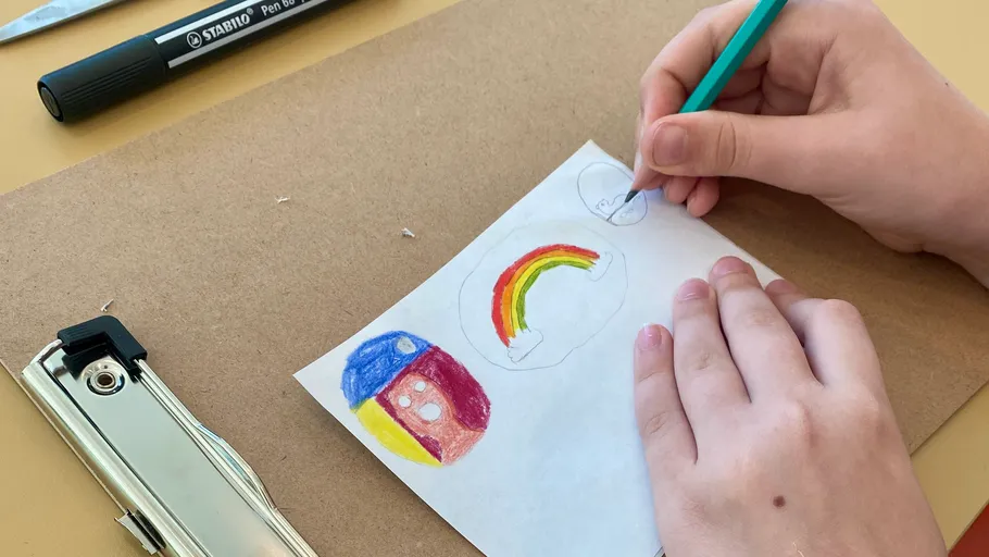 Kind zeichnet Regenbogen auf Klemmbrett.