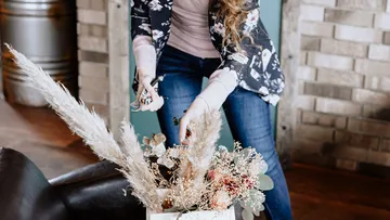 Woman arranging dried flowers in vase indoors.